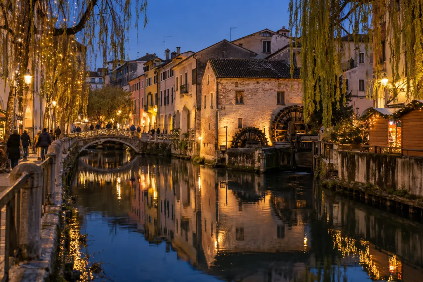 Un canale di Treviso a Natale, con il vecchio mulino dalle ruote ad acqua, i salici piangenti illuminati, il ponte con le luminarie e le case riflesse nell'acqua