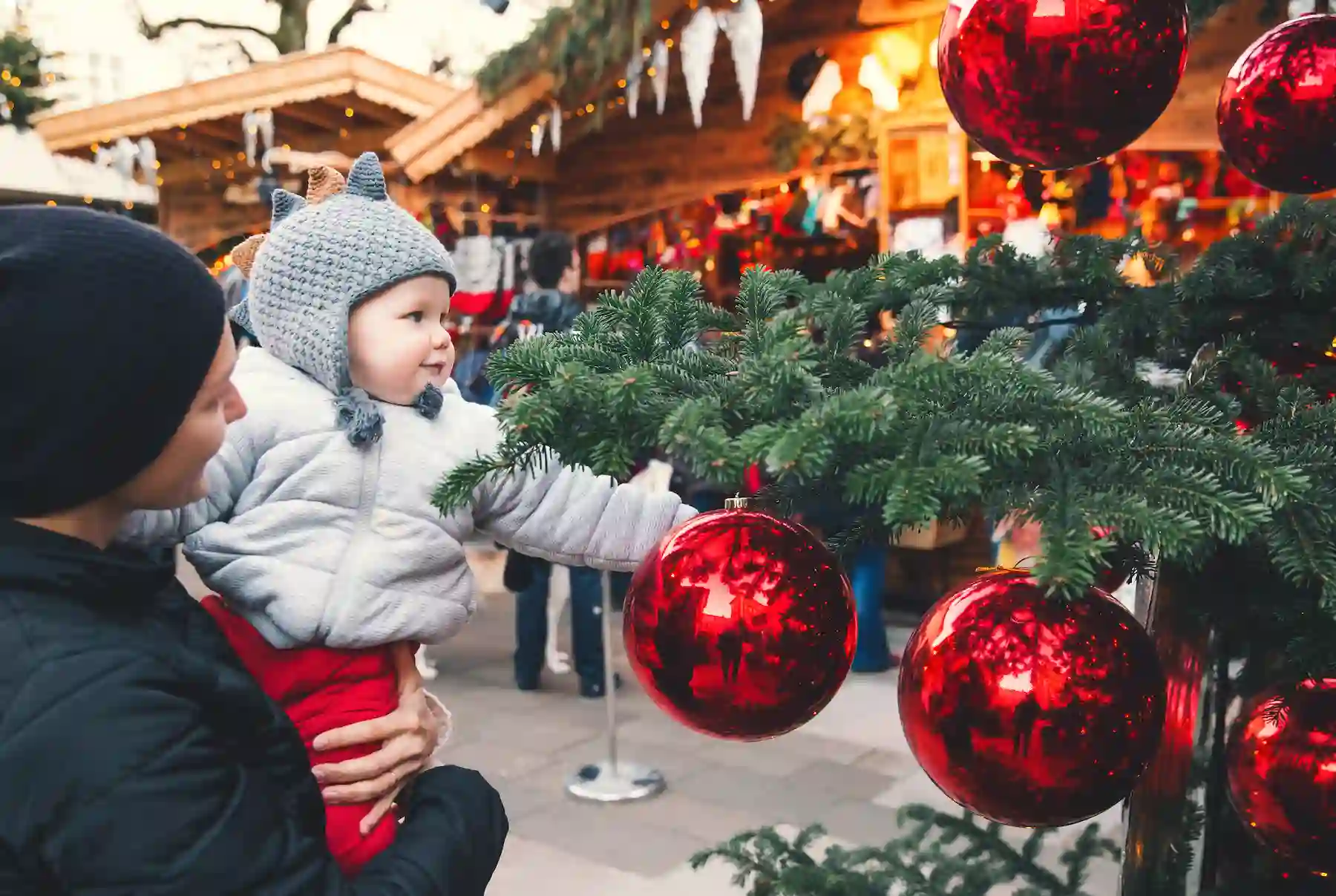 Bambino in braccio a un adulto che tocca una grande pallina rossa su un abete addobbato - mercatini di Natale di Perugia