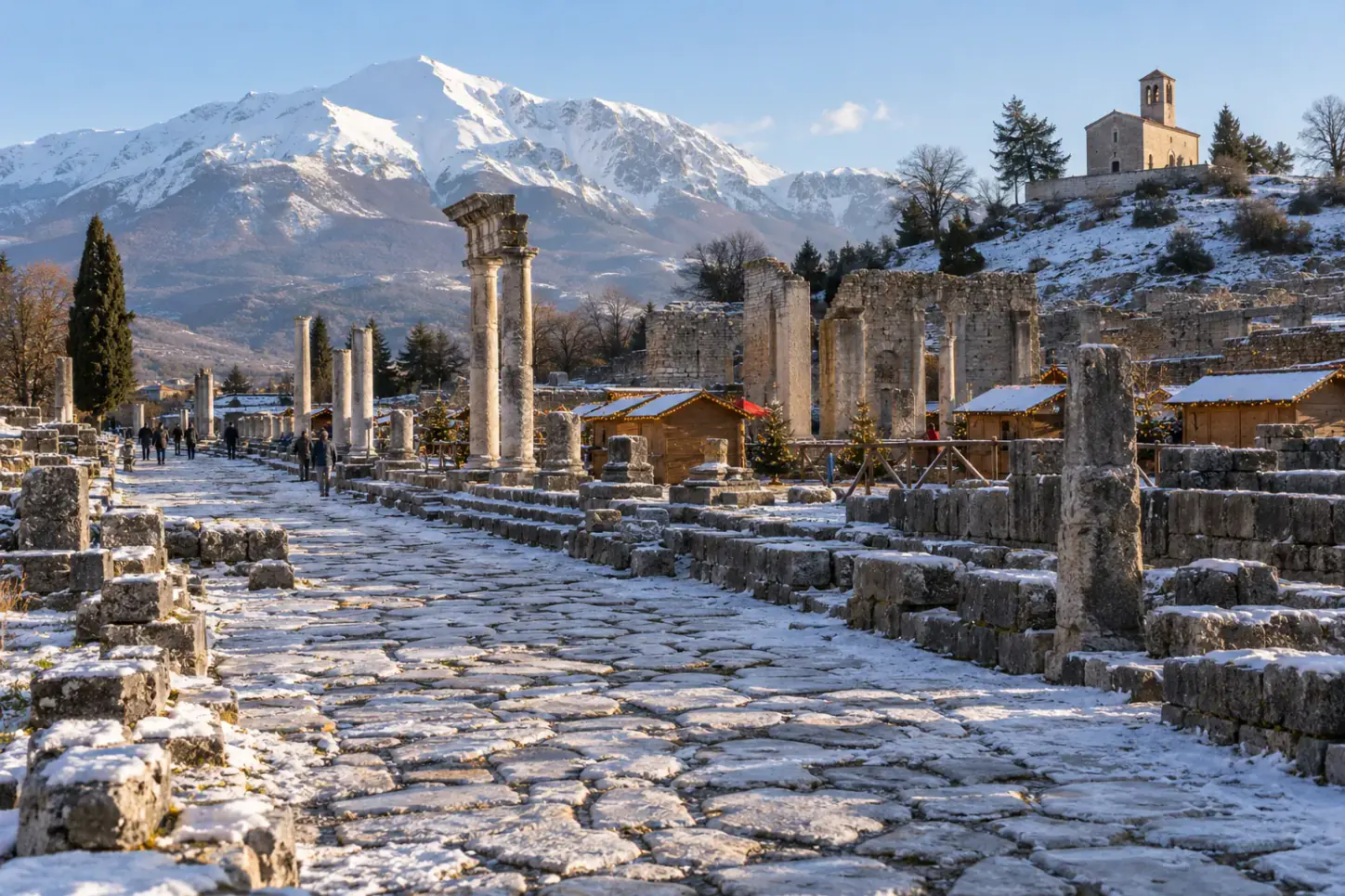 Le rovine romane di Alba Fucens con le casette del mercatino di Natale, le colonne e il Monte Velino innevato sullo sfondo